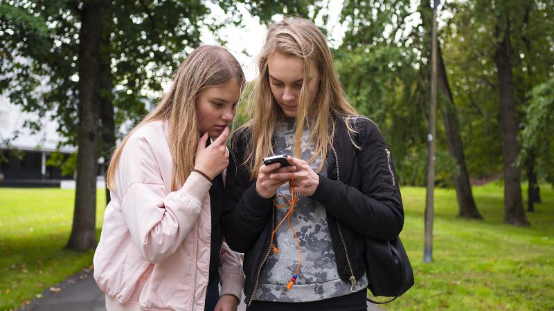 Two teenage girls looking at a mobile phone in a park.