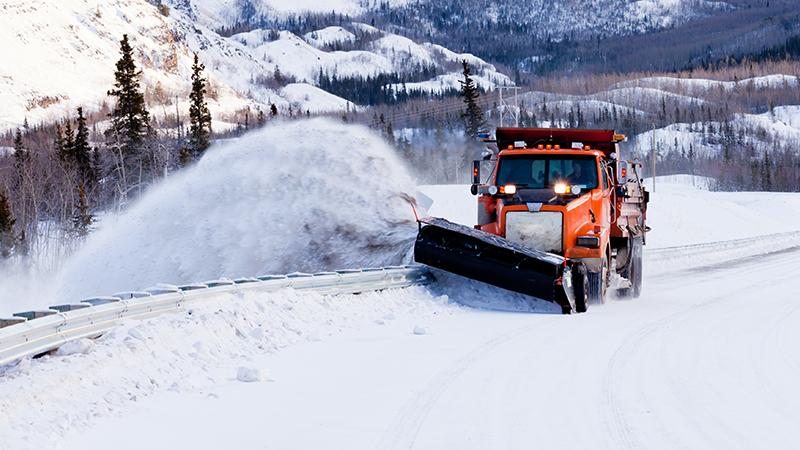 Snow plough truck clearing road after whiteout winter snowstorm blizzard for vehicle access